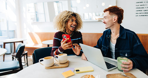 Friends laughing over coffee while working on laptop