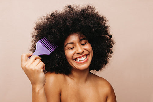 Beautiful woman of color combing her Afro hair in a studio