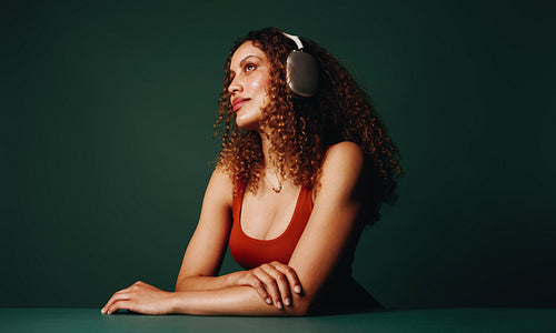Listening in profile, the woman wears headphones in a  color blocking studio setting