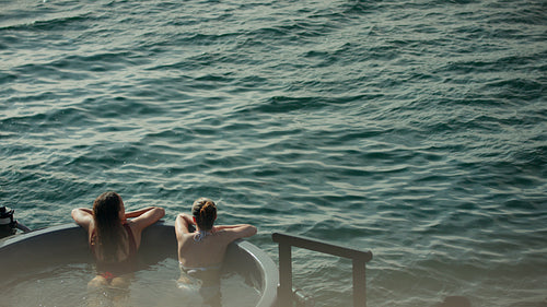 Relaxing women unwind in a hot tub beside the water