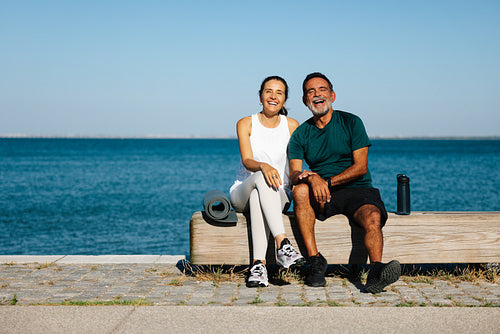 Smiling couple relaxing in workout attire near the peaceful waterfront