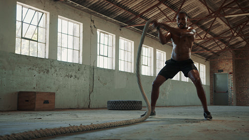 Fitness man exercising with battle rope in a cross training gym