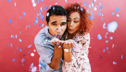 Happy young couple blowing confetti in celebration of their love.