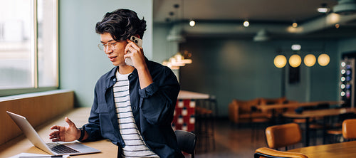 Young professional talking on phone while working on laptop in stylish cafe