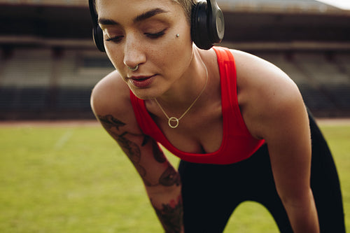 Female athlete standing in a stadium doing workout with hands on knees