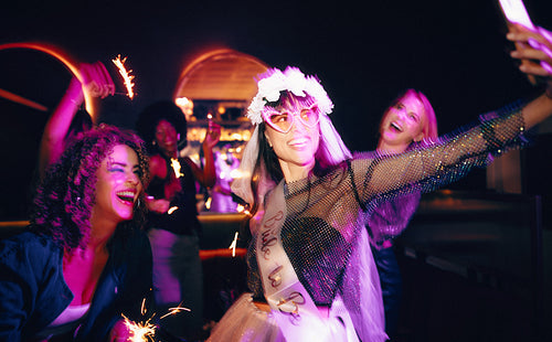 Bride and friends celebrating bachelorette party with sparklers and camera selfies