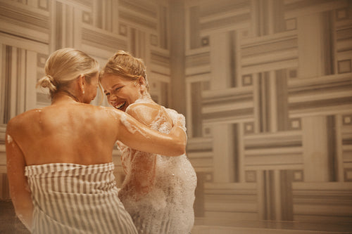 Mature woman and younger woman enjoying time together in a hammam, laughing and having fun