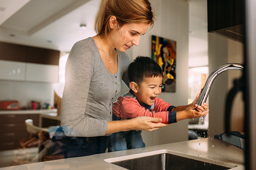 Woman helping little boy to wash hands after cooking