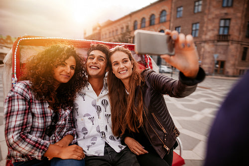 Teenage friends taking selfie on tricycle.