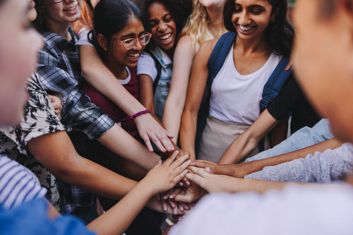 Group of happy teenagers putting their hands together in a huddle