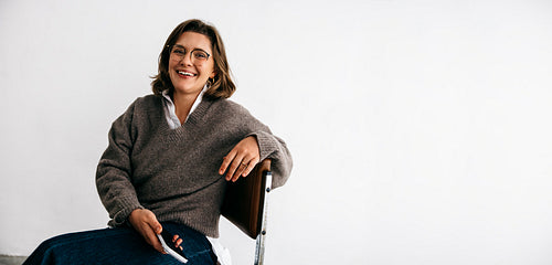 The woman presents a professional profile while sitting with paper on a chair in the studio