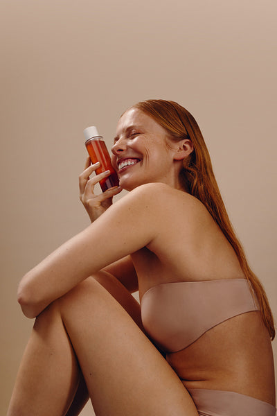 Woman smiling while holding skincare bottle against cheek