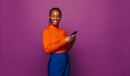 Vibrant girl with two tone braids messaging on smartphone against purple background