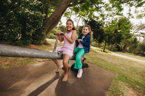 Two young friends playing on a seesaw in a sunny park