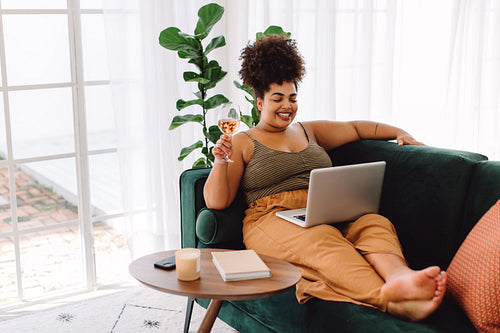 Woman having wine and talking movie on laptop at home