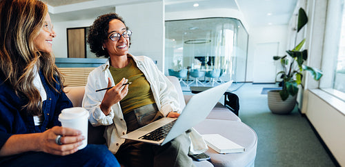 Two women discussing work on a couch in the office