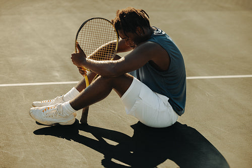 Tennis player sitting and resting with racket on court in sportswear outdoors