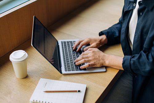 Person using a laptop at a desk with a coffee cup and notebook