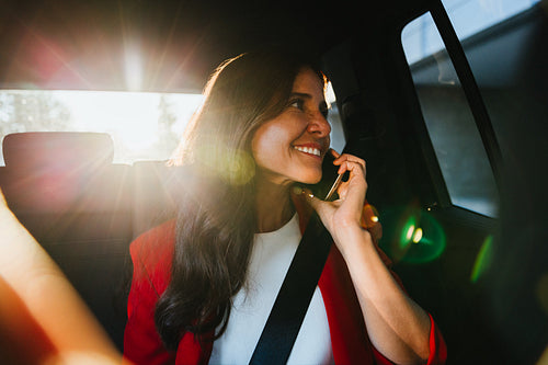 Smiling businesswoman talking on phone in car with sunlight streaming inside