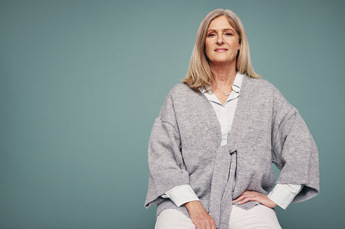 Cheerful senior woman sitting against a studio background