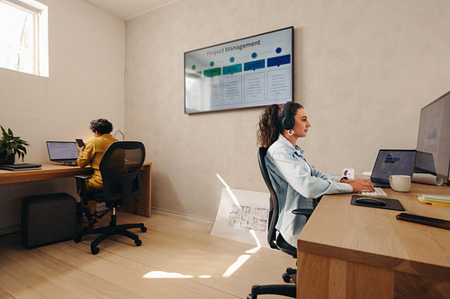 Women working on computers in a modern office with a project board