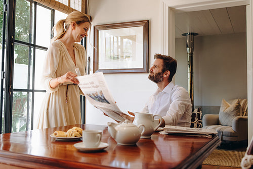 Smiling wife taking away her husband's newspaper inside a hotel