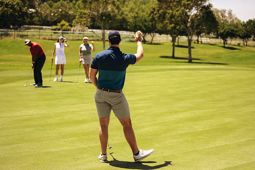 Golfers on putting green with man preparing shot, while teams greet