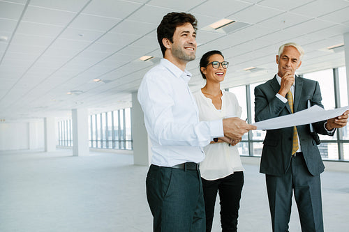 Estate broker and clients discussing over blueprint of new office space