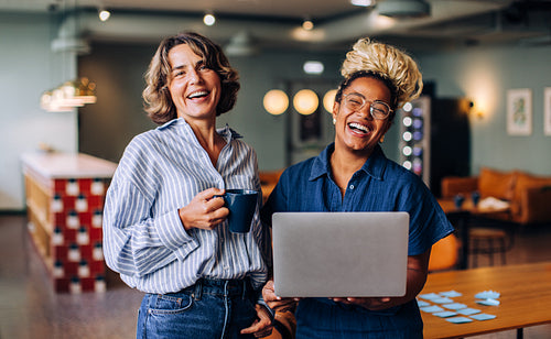 Two friends sharing a laugh while working together with a laptop and coffee