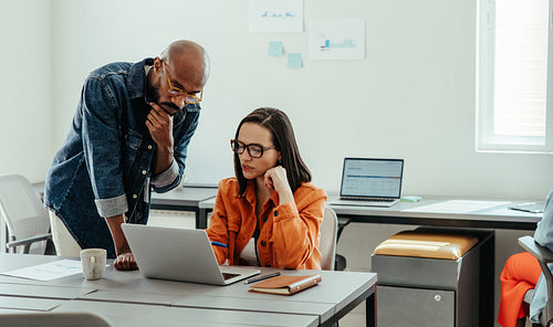Colleagues collaborating in modern office while working on laptop