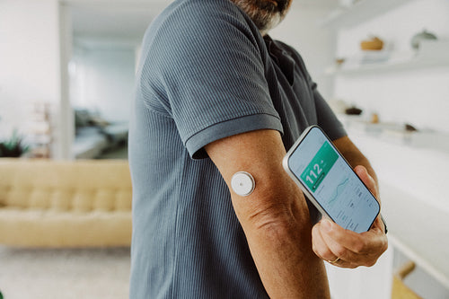 Senior man scans glucose monitor with smartphone at home