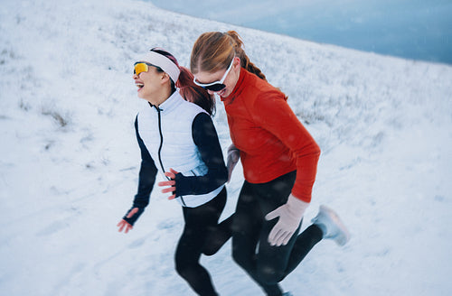 Smiling women are running together on a winter trail with fitness focus