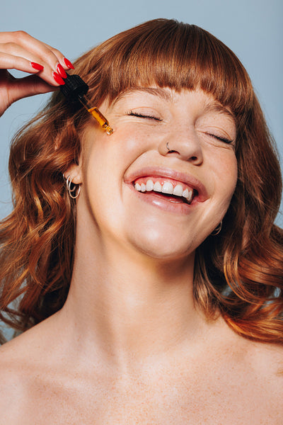 Smiling woman applying face serum with a dropper in a studio