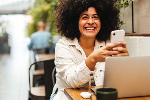 Woman sitting in a cafe, smiling and using a mobile phone