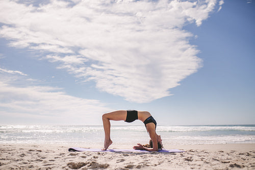 Sporty woman doing back bend at the beach