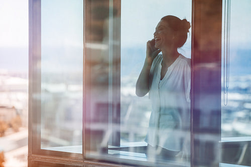 Smiling businesswoman inside office and talking on cell phone