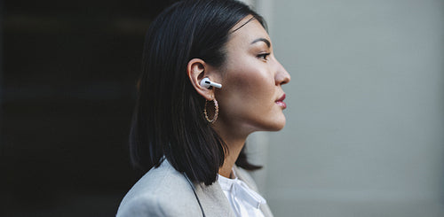 Asian woman listening to music on wireless earphones outdoors