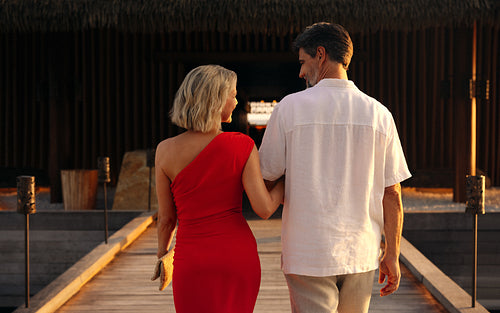 Elegant couple strolling toward resort restaurant at sunset