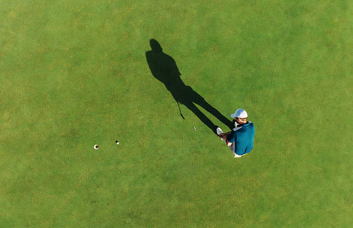Aerial shot of a man taking a golf action shot and putting on the green