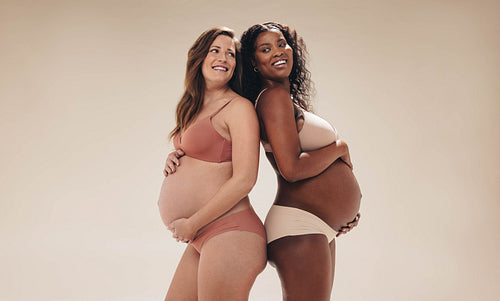 Expecting mothers standing together in lingerie, smiling and celebrating their pregnancy journey