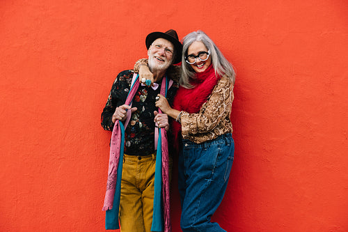 Carefree senior couple laughing together against a red wall