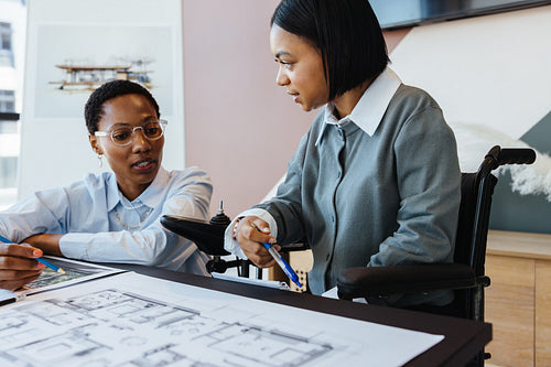 Two young women discussing a design project with plans on the table