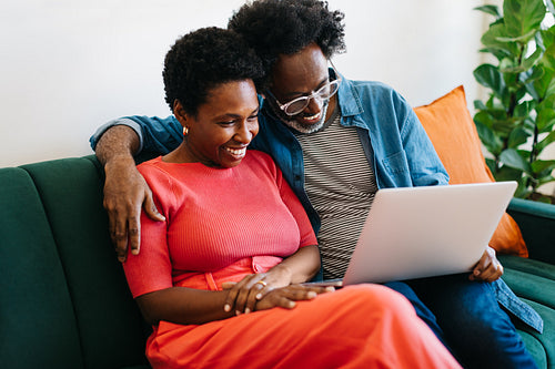 Black couple relaxing at home, smiling and having a video call on a laptop