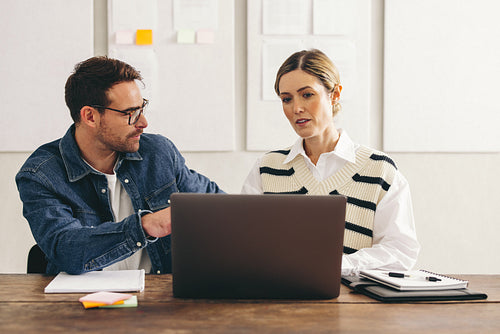 Two young businesspeople working with a laptop in an office