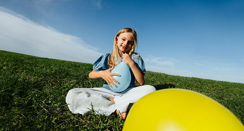 Girl sits on grass with balloon outdoors smiling