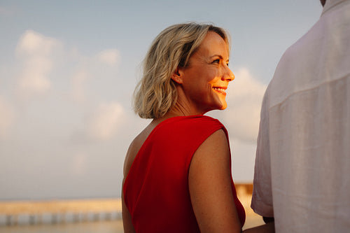 Mature woman smiling at husband in red dress with sunset light outdoors
