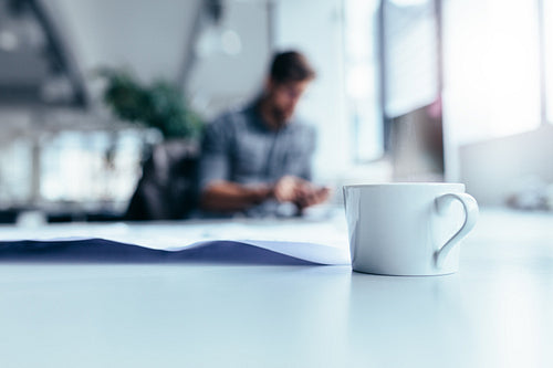 Cup of coffee on desk with man working in background
