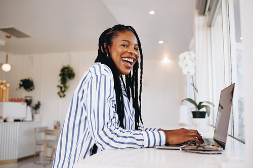 Young female freelancer laughing happily while working on a laptop in a cafe