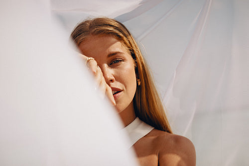 Young woman posing gracefully under soft flowing fabric outdoors in warm sunlight