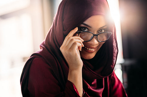 Islamic woman in hijab peeking through eyeglasses